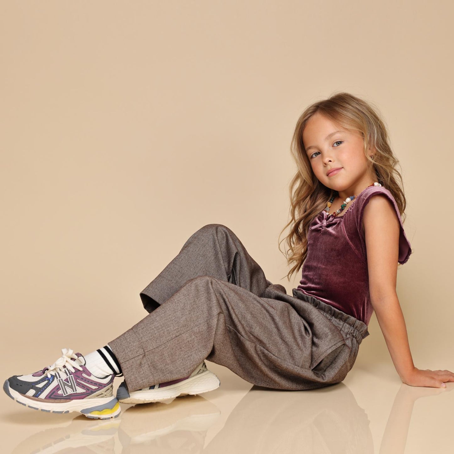 Zittend meisje in stijlvol pakje met witte LilPataz kindersneakers met paarse details – zijaanzicht